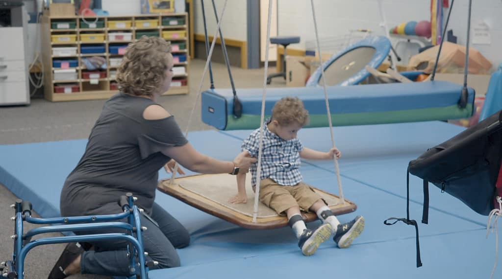 A female occupational therapist working with a young boy on a therapy swing